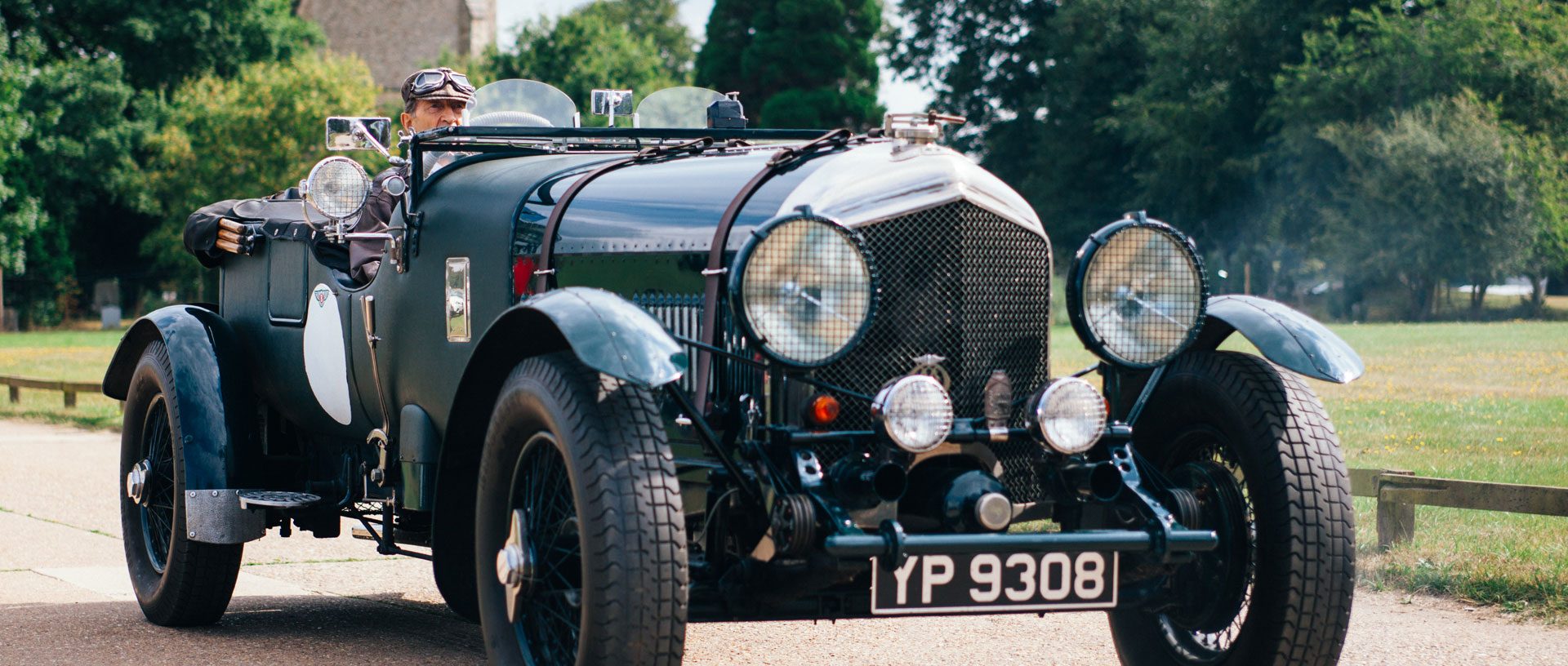 A banner image of a green vintage car with flared wheel arches and two large headlights.
